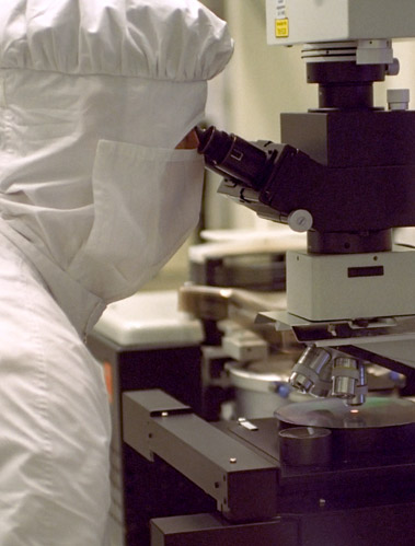 Researcher in safety suit covering everything but their eyes looks through microscope