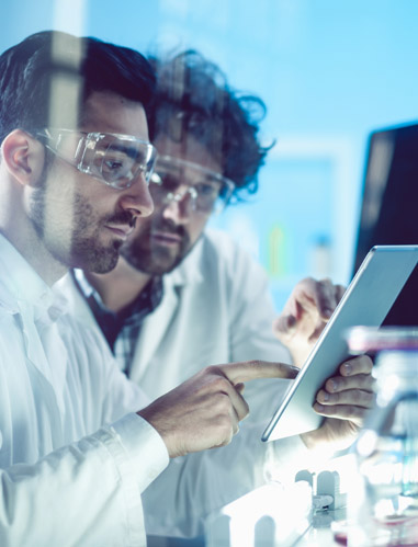 Researchers reviewing tablet in high-tech lab while wearing safety goggles